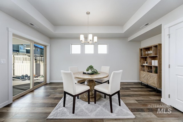 dining room with a raised ceiling, visible vents, dark wood-style floors, and a notable chandelier