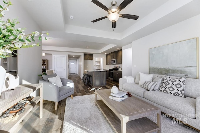 living room featuring recessed lighting, a ceiling fan, a tray ceiling, and dark wood-style flooring