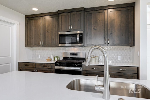 kitchen featuring dark brown cabinets, appliances with stainless steel finishes, a sink, light countertops, and decorative backsplash