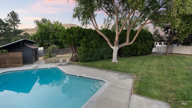 pool at dusk featuring a fenced in pool, a lawn, a patio, a fenced backyard, and a diving board