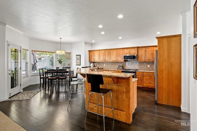 kitchen featuring tasteful backsplash, light stone counters, stainless steel appliances, hanging light fixtures, and an island with sink