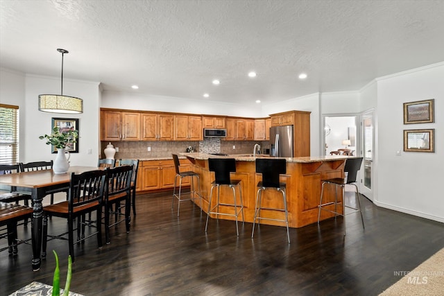 kitchen with decorative backsplash, a kitchen breakfast bar, stainless steel appliances, pendant lighting, and an island with sink