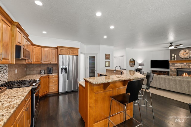 kitchen with a breakfast bar, light stone countertops, an island with sink, a fireplace, and appliances with stainless steel finishes