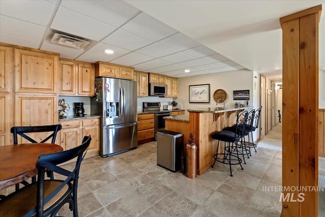 1640 S 5th W, Mountain Home, ID 83647 - kitchen featuring appliances with stainless steel finishes, a breakfast bar area, light stone counters, a paneled ceiling, and light stone finish flooring