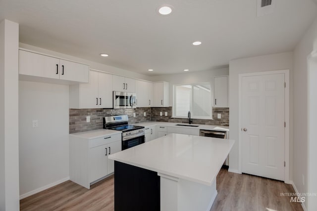 kitchen with white cabinetry, a center island, sink, stainless steel appliances, and light wood-type flooring