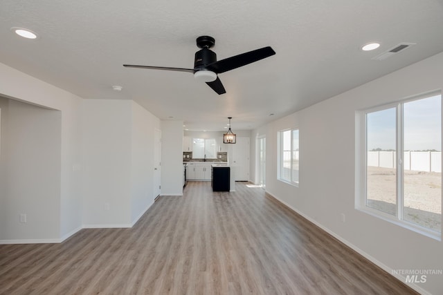 unfurnished living room featuring a textured ceiling, ceiling fan, sink, and light hardwood / wood-style flooring