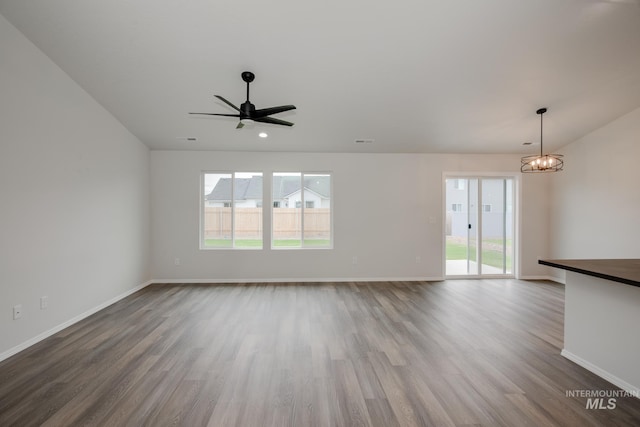 unfurnished living room featuring ceiling fan with notable chandelier, wood finished floors, visible vents, and baseboards