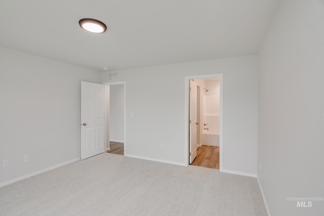 unfurnished bedroom with light colored carpet, visible vents, baseboards, and ensuite bathroom