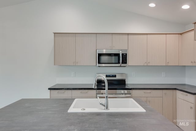 kitchen featuring stainless steel appliances, dark countertops, recessed lighting, light brown cabinets, and vaulted ceiling