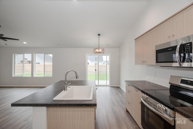 kitchen with dark countertops, a center island with sink, appliances with stainless steel finishes, and a sink