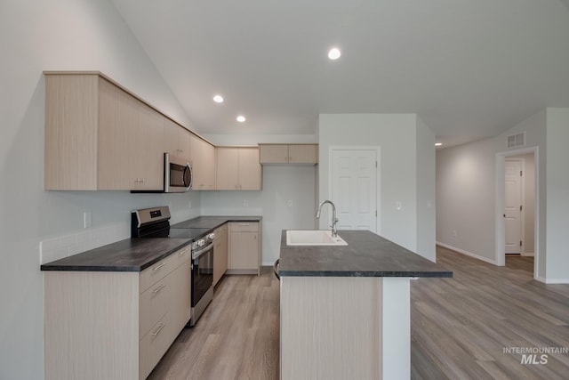 kitchen featuring dark countertops, appliances with stainless steel finishes, a sink, and an island with sink