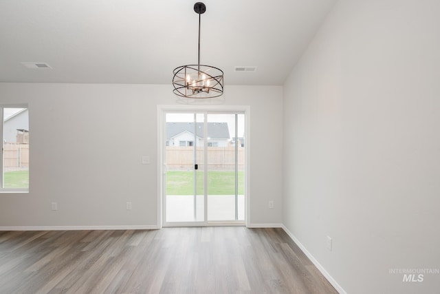 empty room featuring light wood-style flooring, visible vents, a chandelier, and baseboards