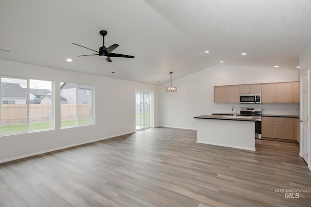 kitchen with dark countertops, appliances with stainless steel finishes, open floor plan, light brown cabinets, and pendant lighting