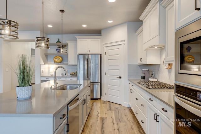 kitchen with pendant lighting, stainless steel appliances, light wood-style floors, white cabinets, and a sink