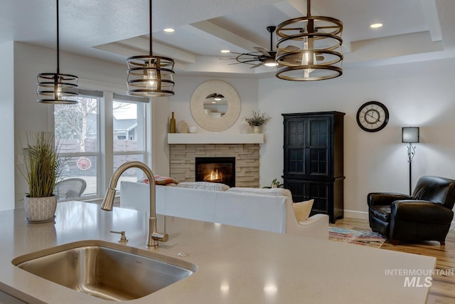 kitchen featuring a tray ceiling, a fireplace, recessed lighting, a sink, and wood finished floors