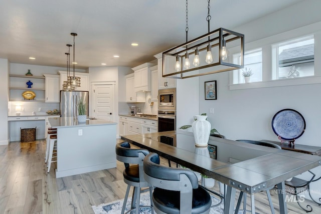 kitchen with appliances with stainless steel finishes, a breakfast bar area, light wood-type flooring, white cabinetry, and open shelves