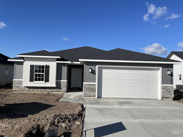 prairie-style home featuring driveway, stone siding, roof with shingles, and an attached garage