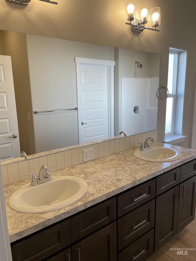 bathroom featuring tiled shower, a sink, an inviting chandelier, and double vanity