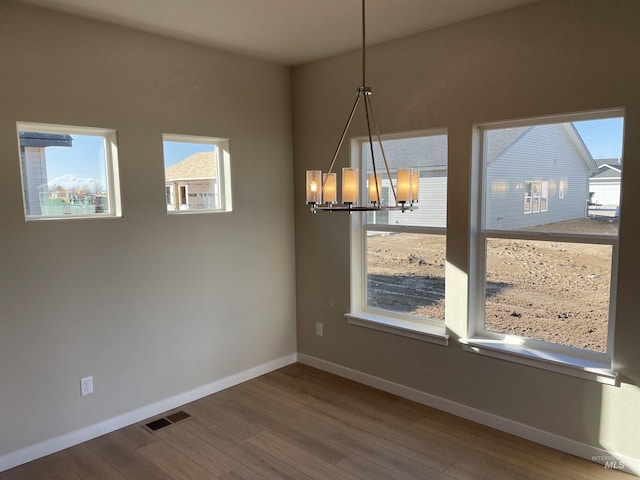 unfurnished dining area with visible vents, baseboards, a chandelier, and wood finished floors