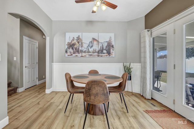 dining room with light wood-style floors, ceiling fan, stairway, and arched walkways