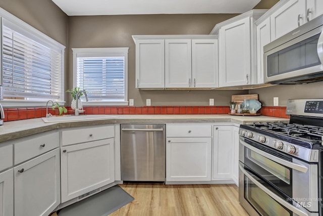 kitchen featuring light wood finished floors, stainless steel appliances, light countertops, white cabinets, and a sink