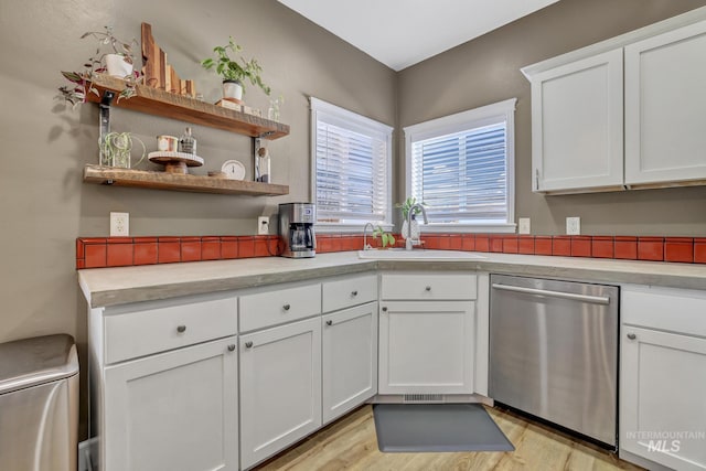 kitchen featuring light wood finished floors, light countertops, stainless steel dishwasher, white cabinets, and a sink