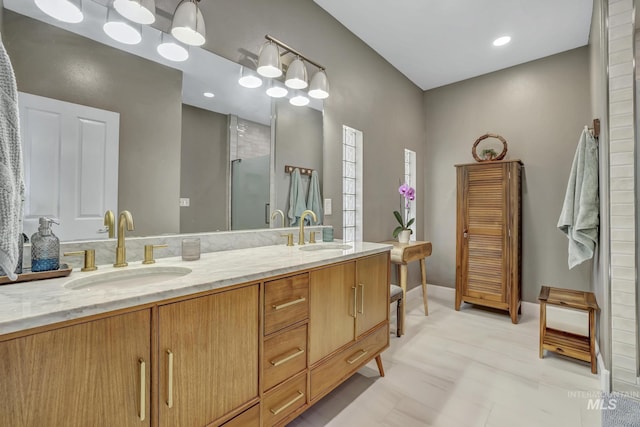 bathroom featuring double vanity, a shower with door, baseboards, and a sink