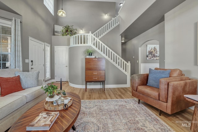 living room featuring a towering ceiling, stairway, arched walkways, and wood finished floors