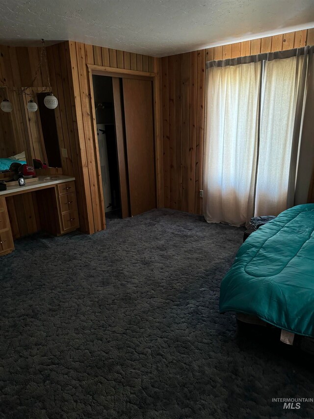 carpeted bedroom with a textured ceiling, wood walls, and a closet