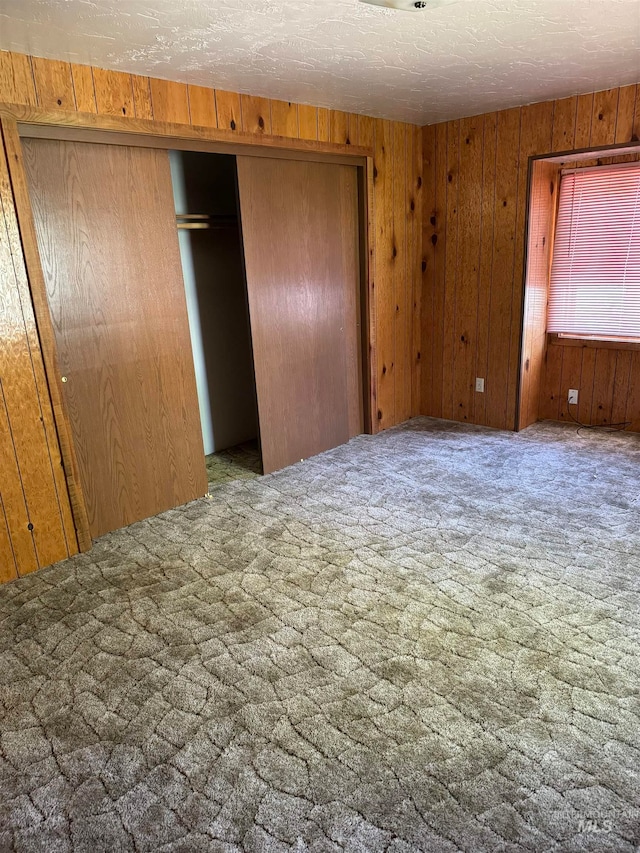 unfurnished bedroom with a textured ceiling, light colored carpet, a closet, and wooden walls