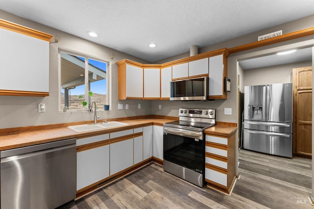 kitchen with light countertops, appliances with stainless steel finishes, dark wood-style floors, white cabinetry, and a sink