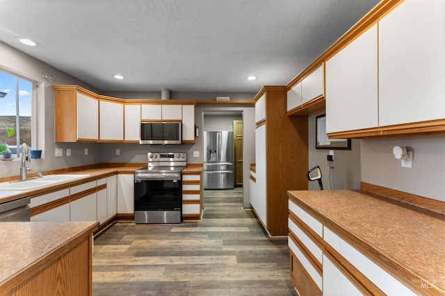 kitchen with recessed lighting, dark wood-style flooring, a sink, stainless steel appliances, and white cabinets