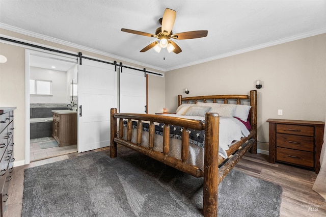 bedroom featuring wood finished floors, ensuite bath, a sink, ornamental molding, and a barn door