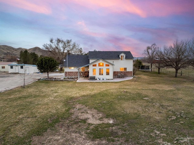 back of property at dusk with a mountain view, a lawn, and a patio area