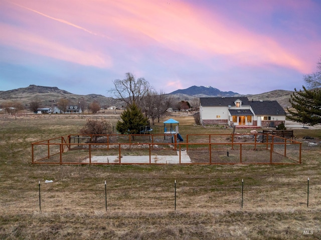 playground at dusk featuring fence, a garden, a rural view, a playground, and a mountain view