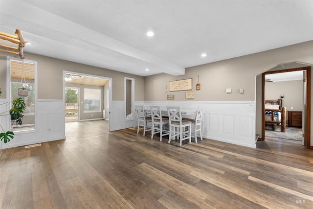 dining space with beam ceiling, recessed lighting, wood finished floors, and a wainscoted wall