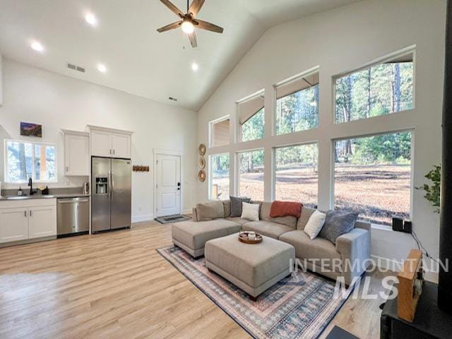 living area with visible vents, high vaulted ceiling, a ceiling fan, light wood-style floors, and baseboards