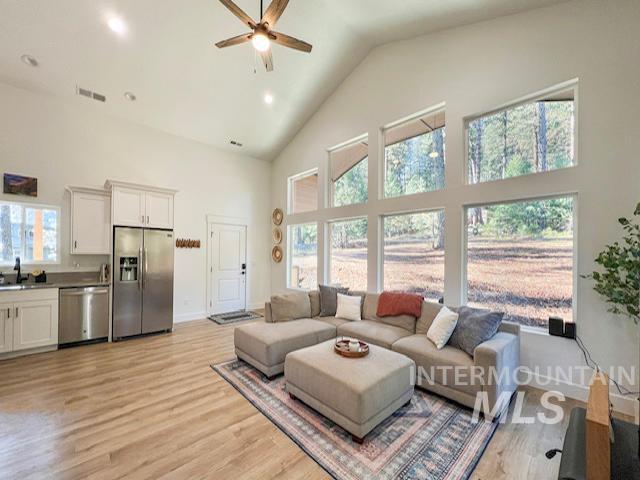 living area featuring visible vents, baseboards, light wood-style floors, high vaulted ceiling, and a ceiling fan