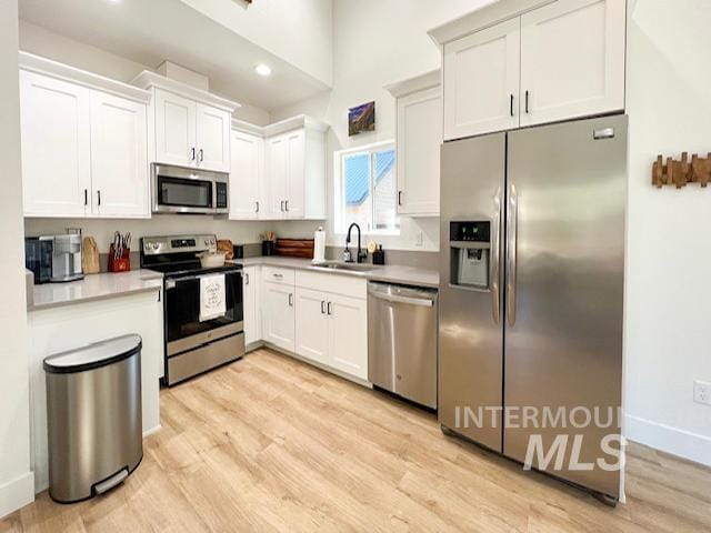 kitchen featuring baseboards, light wood finished floors, a sink, stainless steel appliances, and white cabinetry