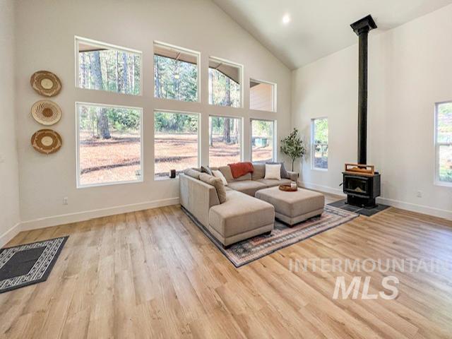 living room with baseboards, high vaulted ceiling, wood finished floors, and a wood stove