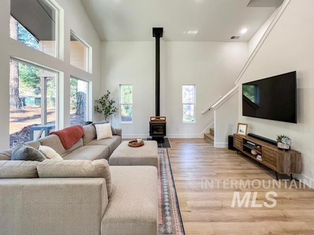 living area featuring light wood-type flooring, stairway, baseboards, a towering ceiling, and a wood stove