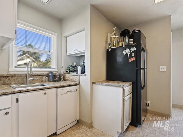 kitchen featuring baseboards, white dishwasher, freestanding refrigerator, a sink, and white cabinetry
