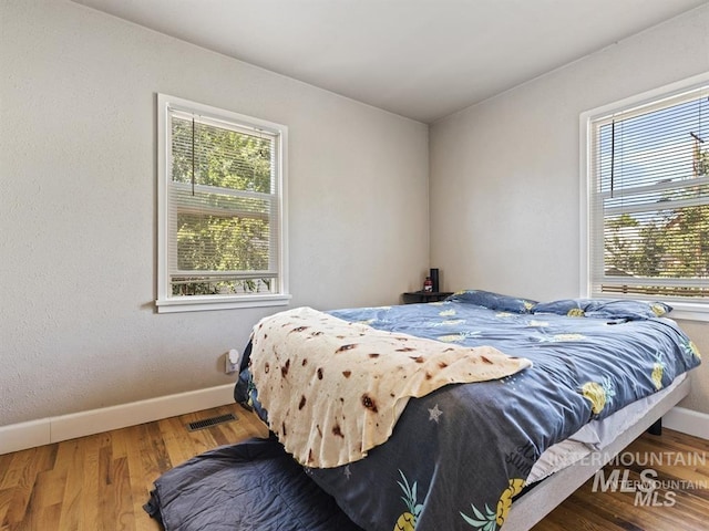 bedroom with baseboards, multiple windows, visible vents, and wood finished floors