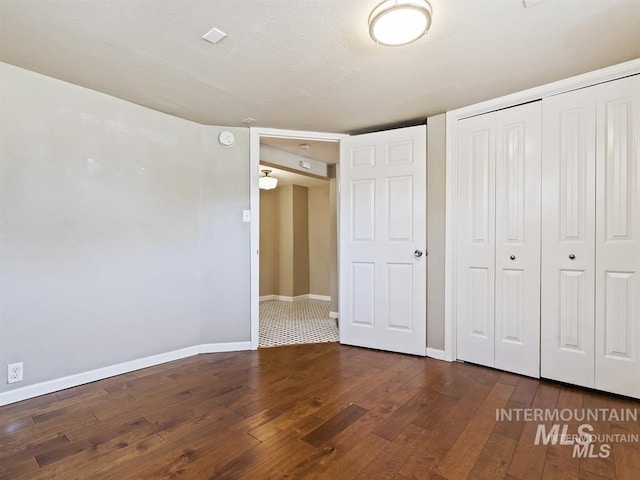 unfurnished bedroom with dark wood-style floors, baseboards, a closet, and a textured ceiling