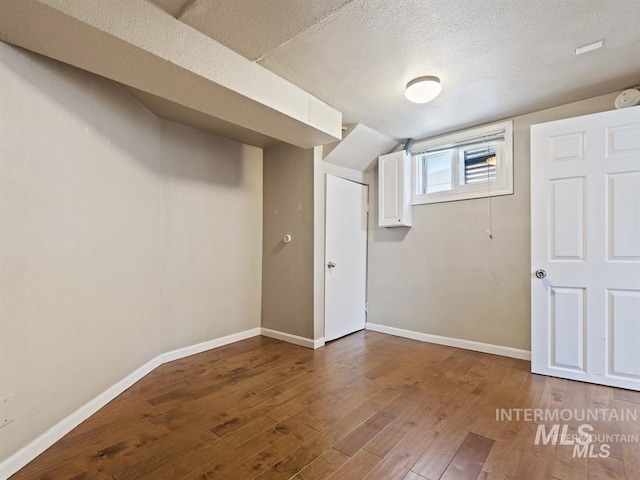 basement featuring baseboards, wood-type flooring, and a textured ceiling