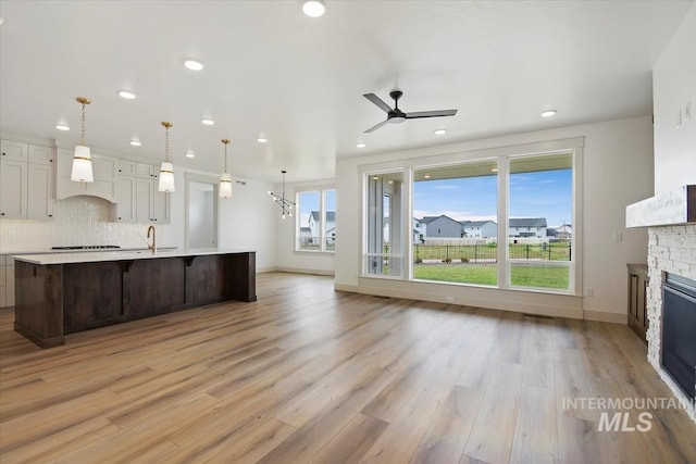 kitchen featuring a fireplace, light wood-type flooring, custom exhaust hood, sink, and decorative backsplash