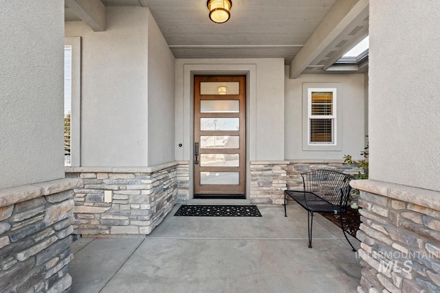 entrance to property featuring a porch, stone siding, and stucco siding