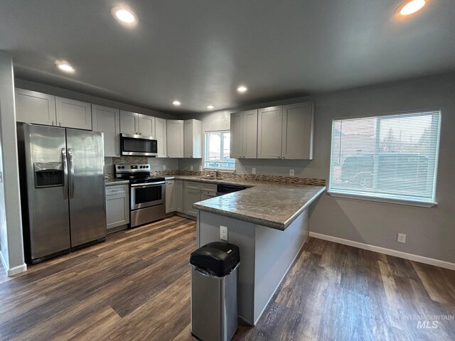 kitchen featuring dark hardwood / wood-style flooring, a kitchen bar, sink, kitchen peninsula, and stainless steel appliances