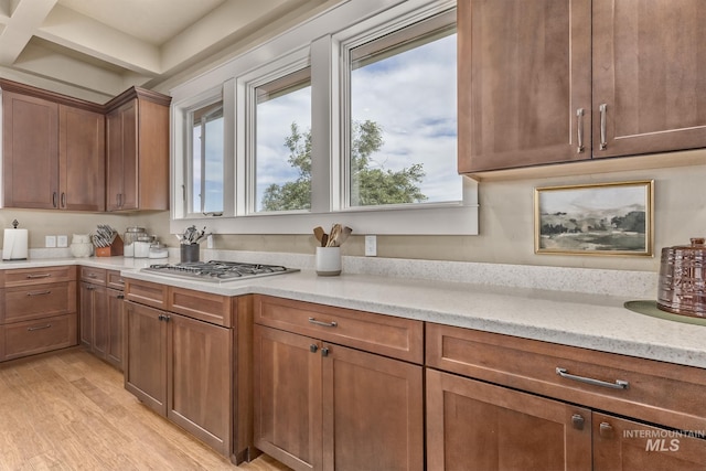 kitchen with light wood-style flooring, plenty of natural light, light countertops, stainless steel gas stovetop, and beamed ceiling