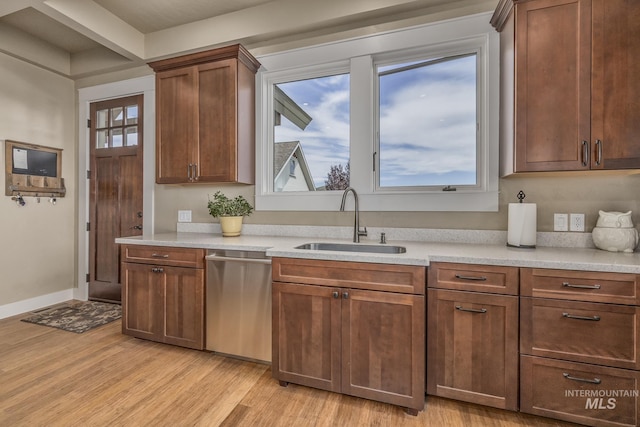 kitchen featuring a sink, stainless steel dishwasher, light wood-style floors, and light countertops